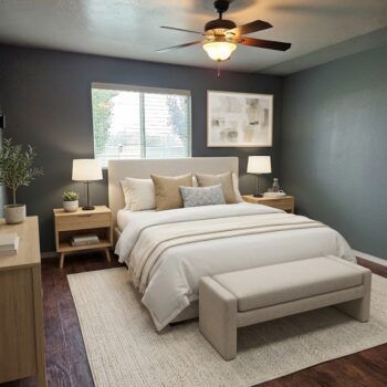 A bedroom with dark blue walls, a light-colored bed with neutral bedding, matching nightstands, and a light-colored bench.
