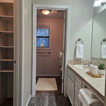 A bathroom with a linen closet on the left, a vanity with a sink and towels on the right, and a separate water closet.