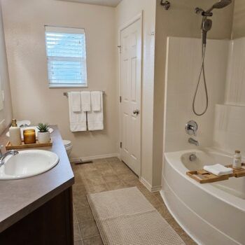 A neutral-toned bathroom with a vanity, a bathtub shower combination, and white towels hanging on the wall.