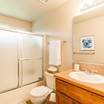 A clean, bright bathroom with a light wood vanity, a white porcelain sink, a toilet, and a walk-in shower with glass doors.