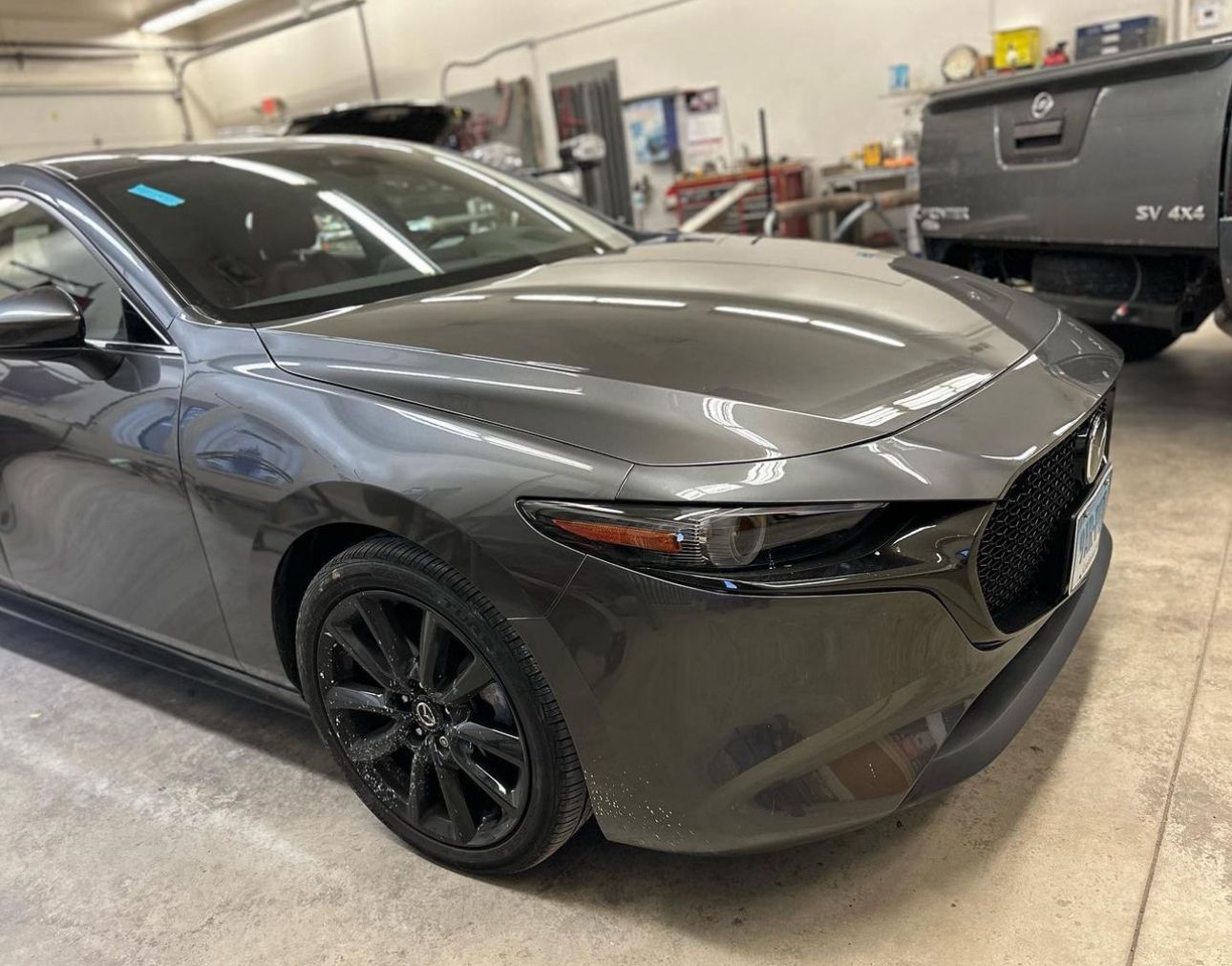 A gray car with a damaged hood is parked in a garage after