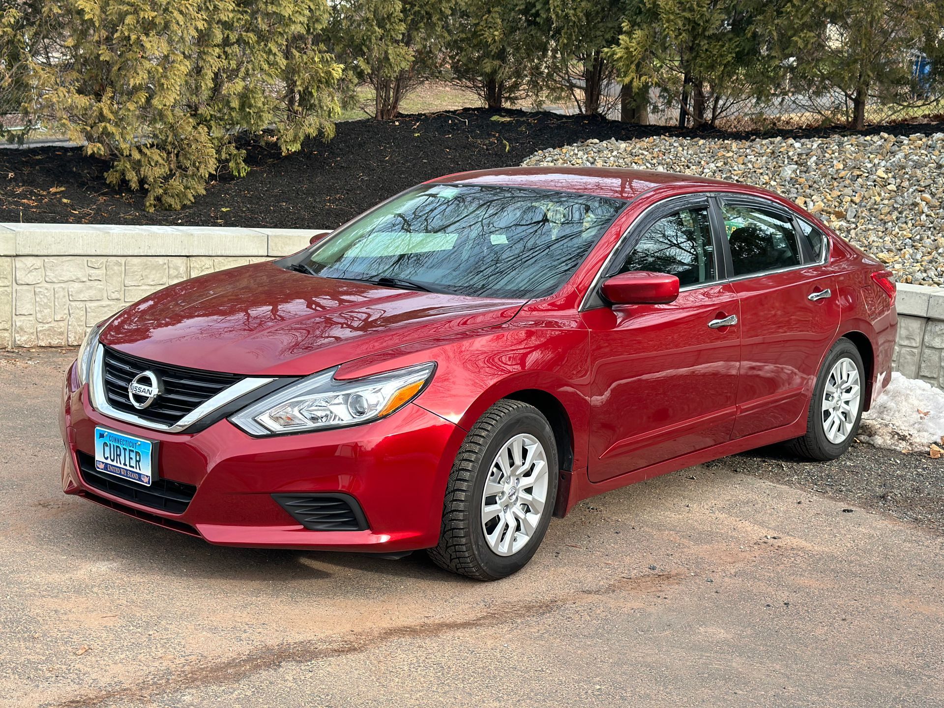 A red nissan altima is parked in a parking lot after