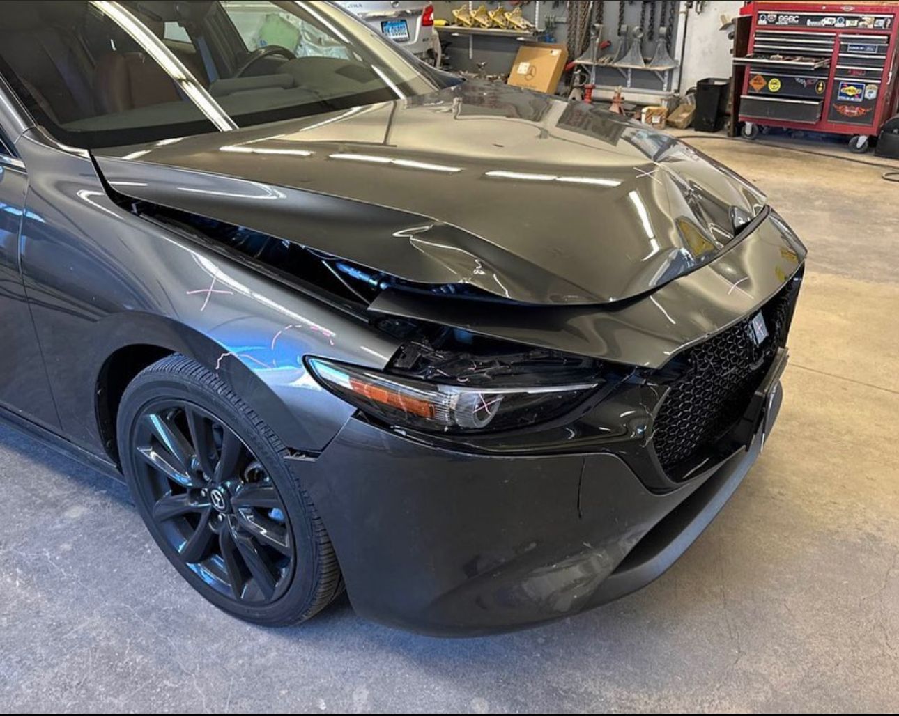 A gray car with a damaged hood is parked in a garage before