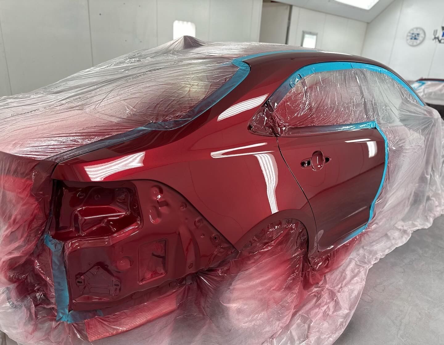 A red car is being painted in a paint booth.