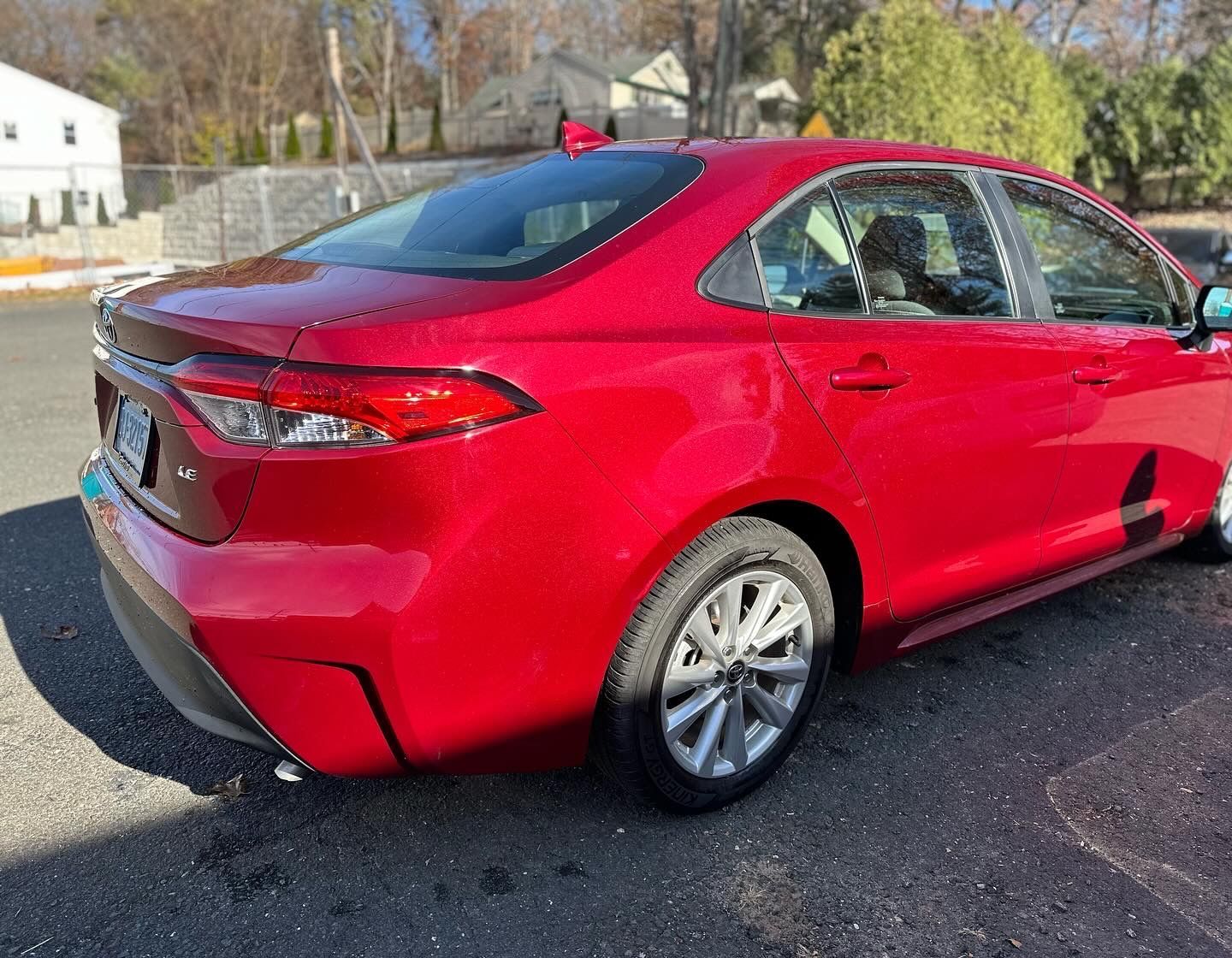 A red toyota corolla is parked on the side of the road.