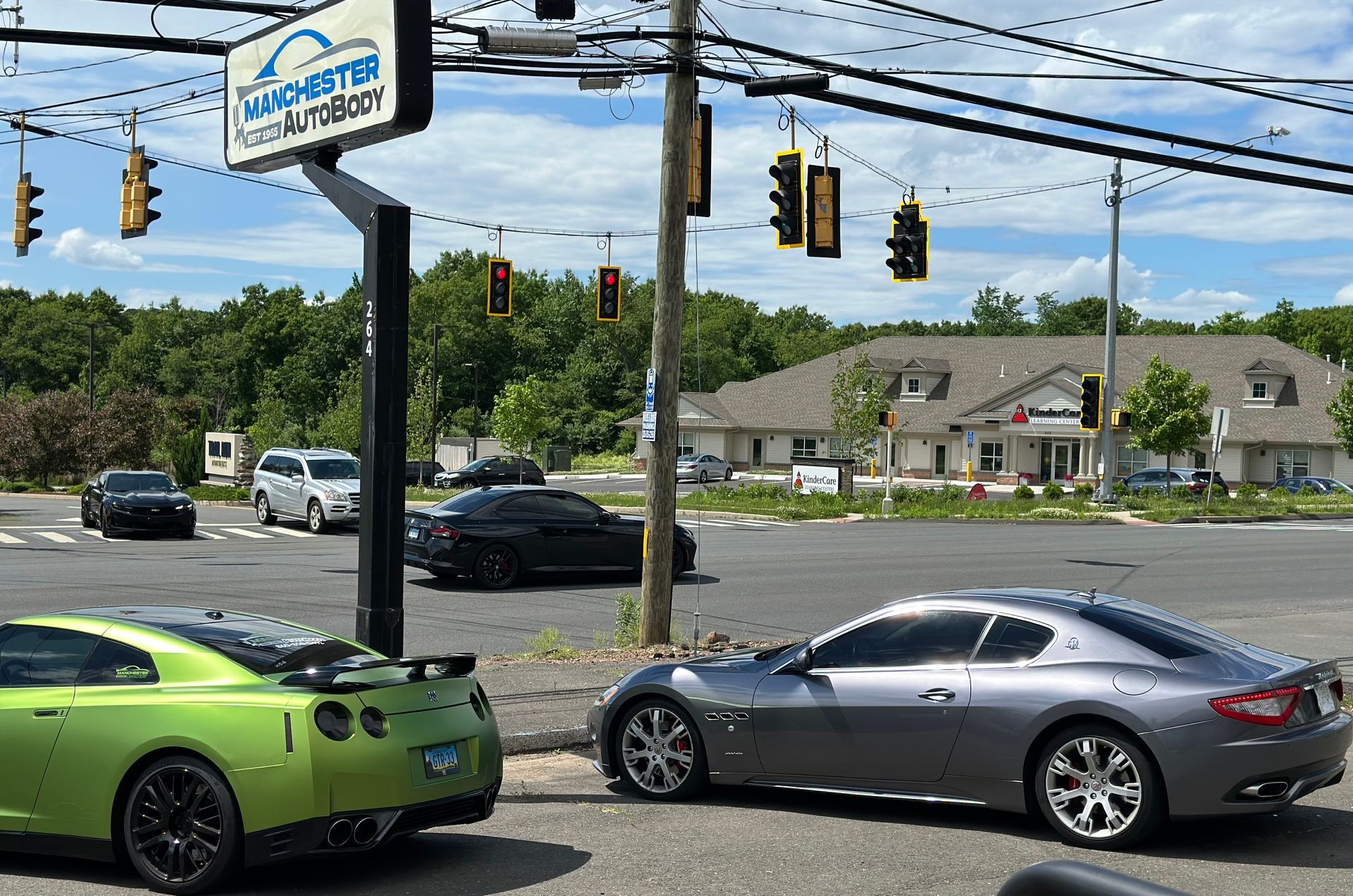 Two sports cars are parked on the side of the road in front of a car dealership.