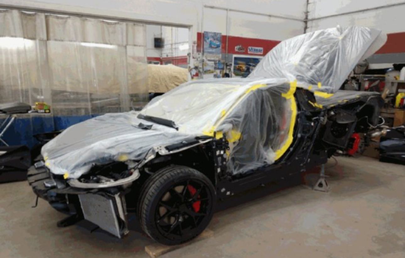 A car is wrapped in plastic and sitting in a garage.