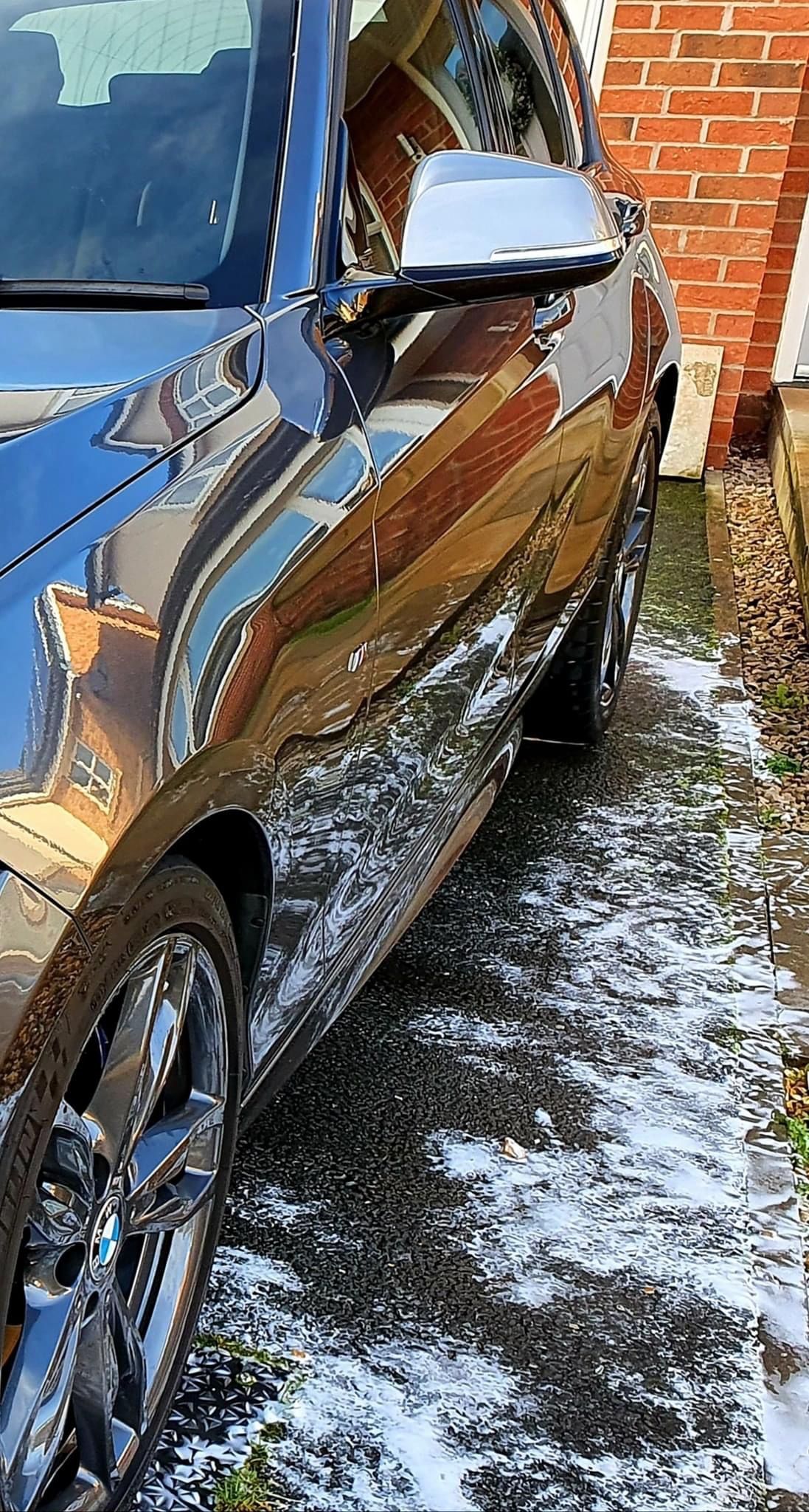 A black car is parked in the snow in front of a brick building.