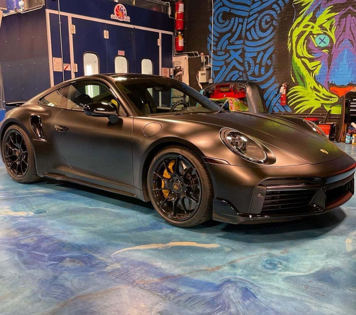 A black porsche 911 turbo s is parked in a garage.
