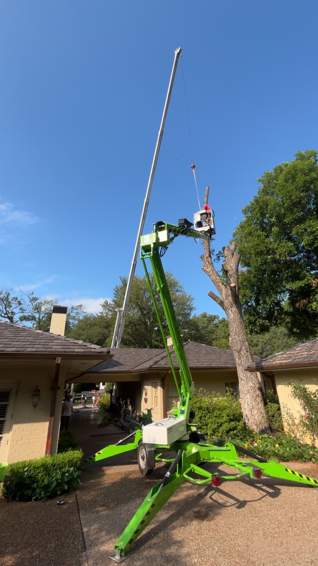 Green crane lifting a tall striped pole beside a house under a clear blue sky