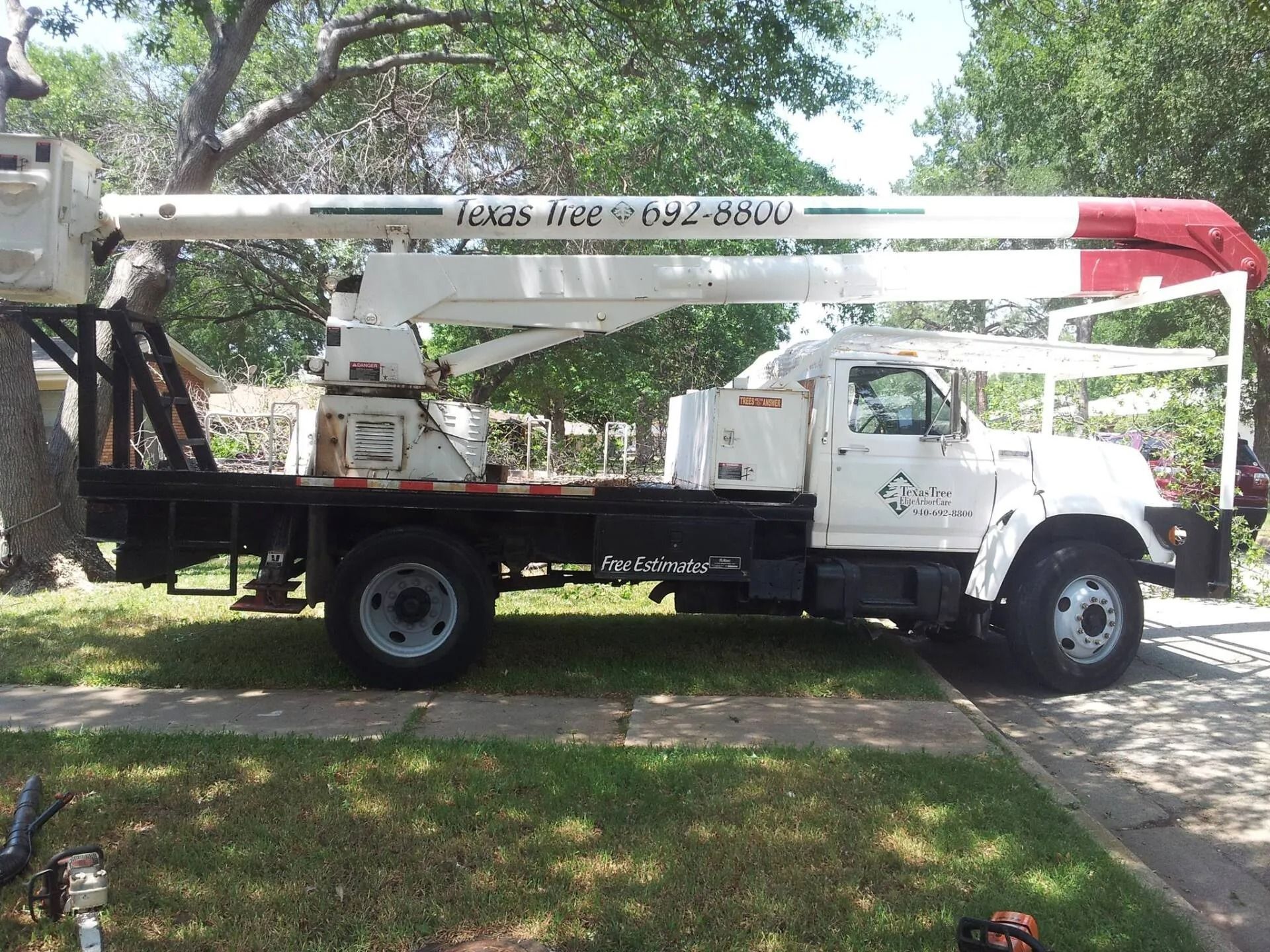 White tree service truck with extended boom, parked on a residential street.