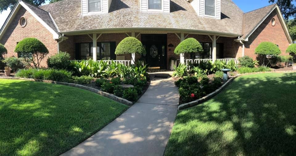 Brick house with a curved porch, lush landscaping, and a concrete pathway leading to the front door.