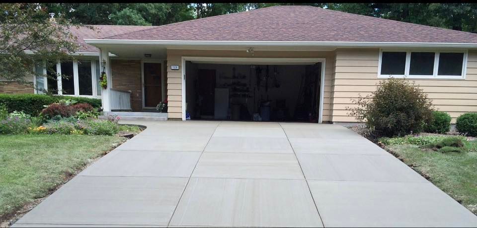 A beige ranch-style house with a brown roof and a freshly poured, smooth concrete driveway leading to an open garage.