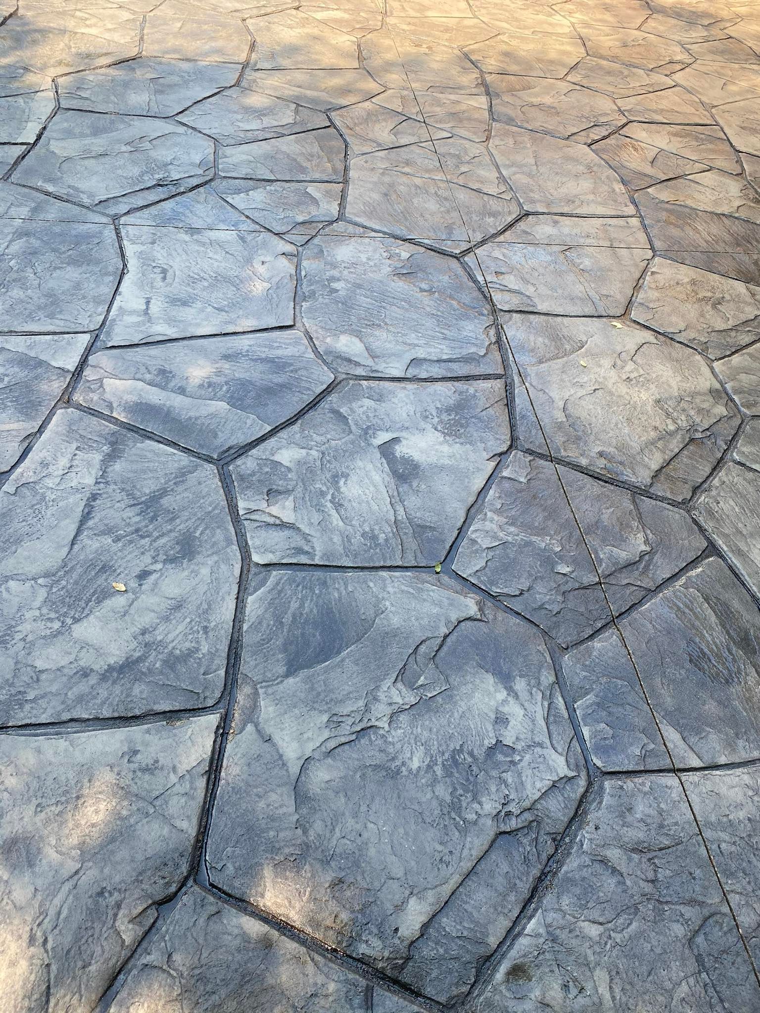 Close-up of a gray stamped concrete patio with a random, natural stone pattern and dark grout lines.