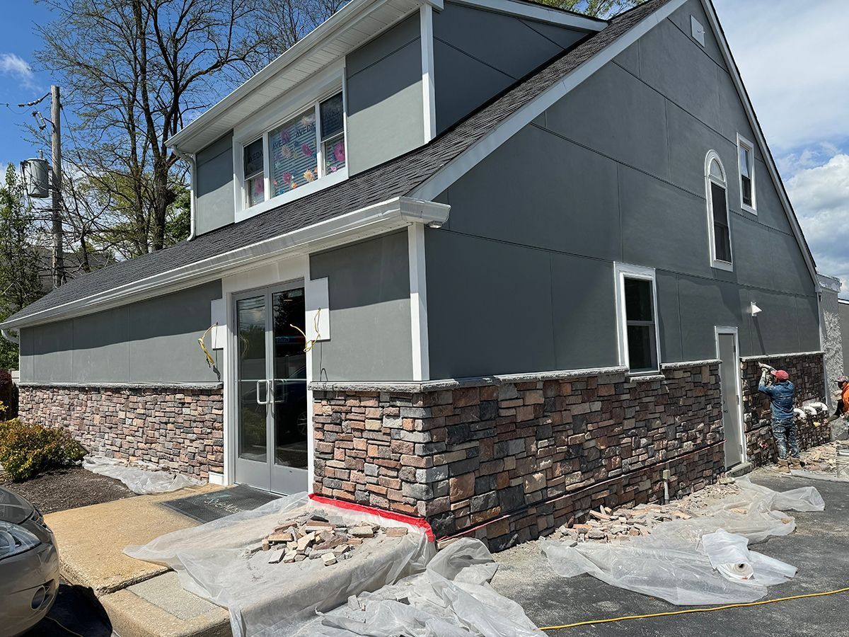 Building exterior with stone veneer and gray siding. A worker is visible.