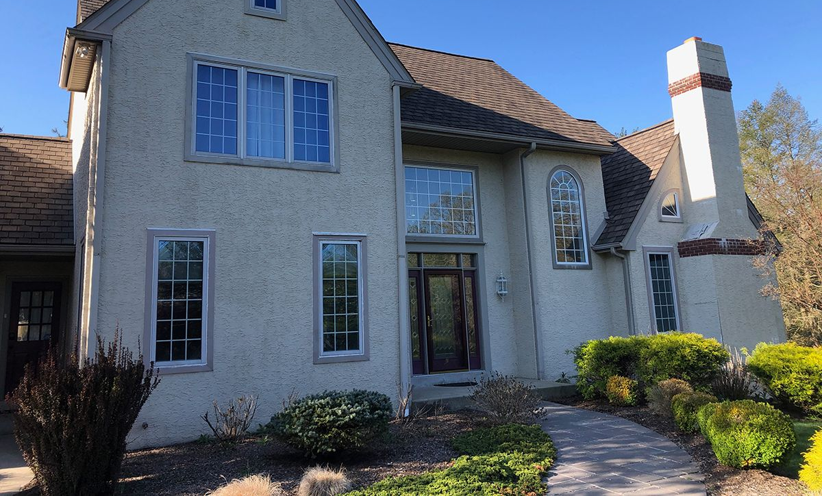 Two-story stucco house with brown roof and tall chimney; blue sky in background.