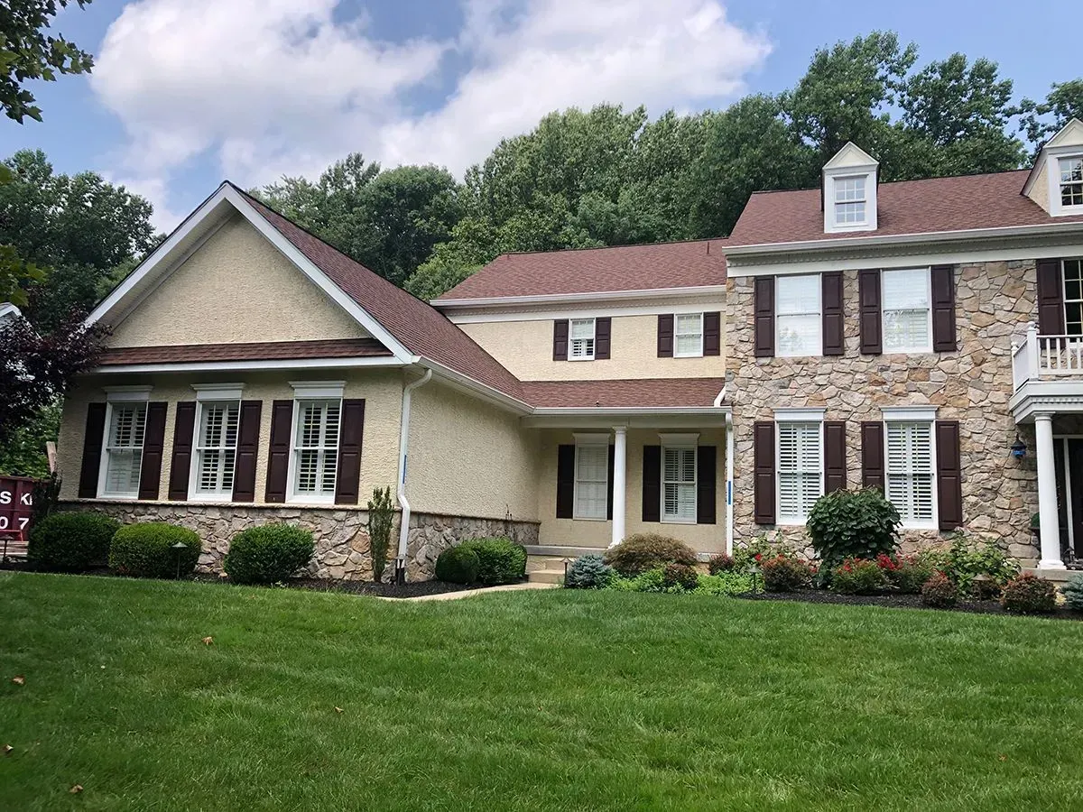 Two-story house with stone and stucco facade, brown shutters, and green lawn.