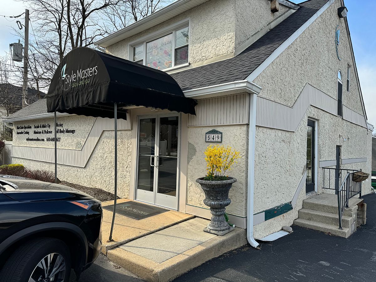 Exterior of a light-colored building with a black awning over the entrance. A car is parked on the left.