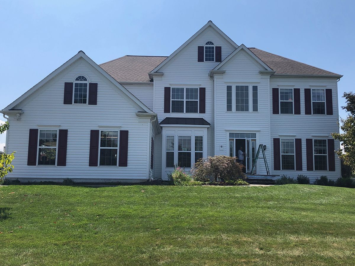 White house with maroon shutters and a green lawn under a blue sky.