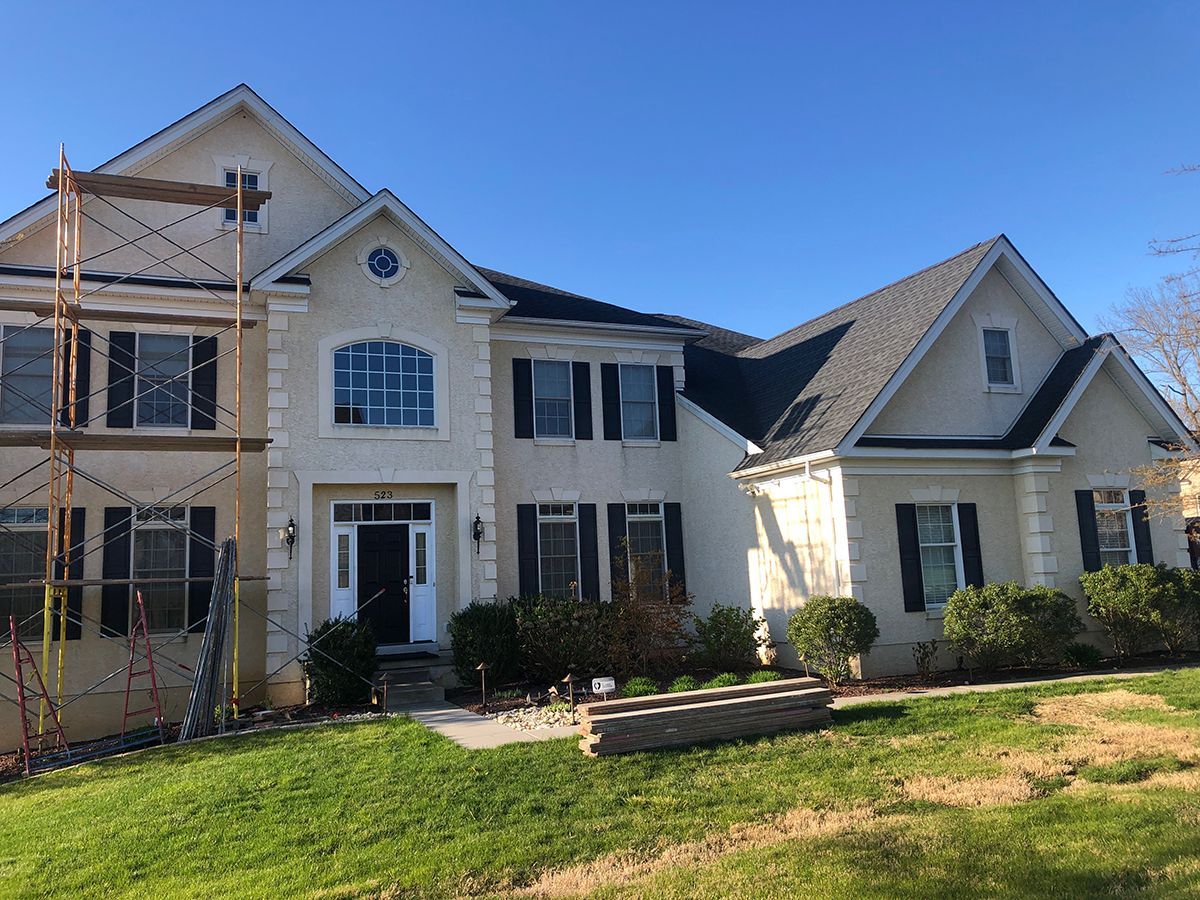 House exterior with stucco siding, black shutters, and dark roof under a clear blue sky.
