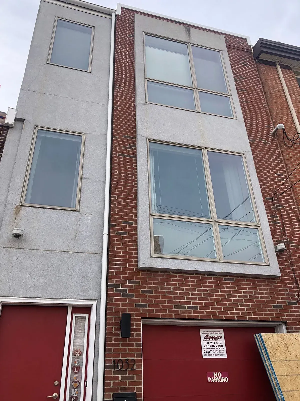 Three-story townhouses. One gray stucco, red door. The other brick, red garage door, and large windows.