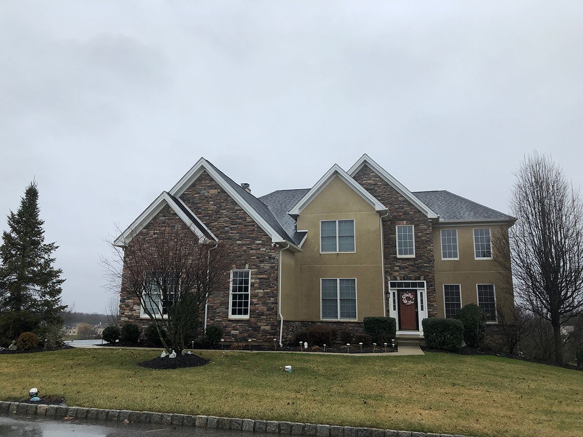 Two-story house with stone and stucco facade, a dark roof, and a red front door under a cloudy sky.