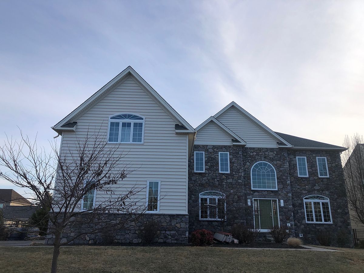 Two-story house with light siding and stone facade under a cloudy sky.
