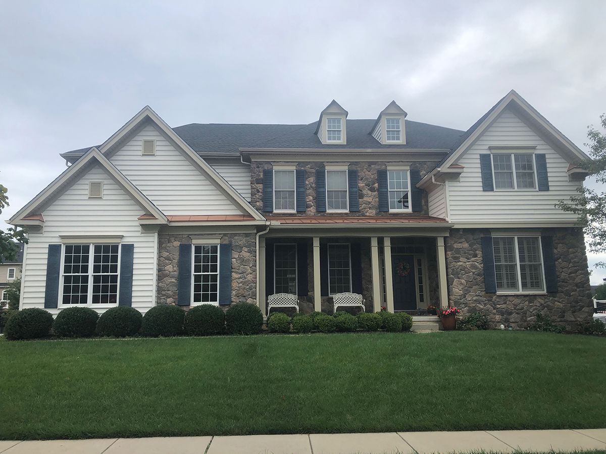 Two-story house with stone facade, white siding, blue shutters, and green lawn under a cloudy sky.