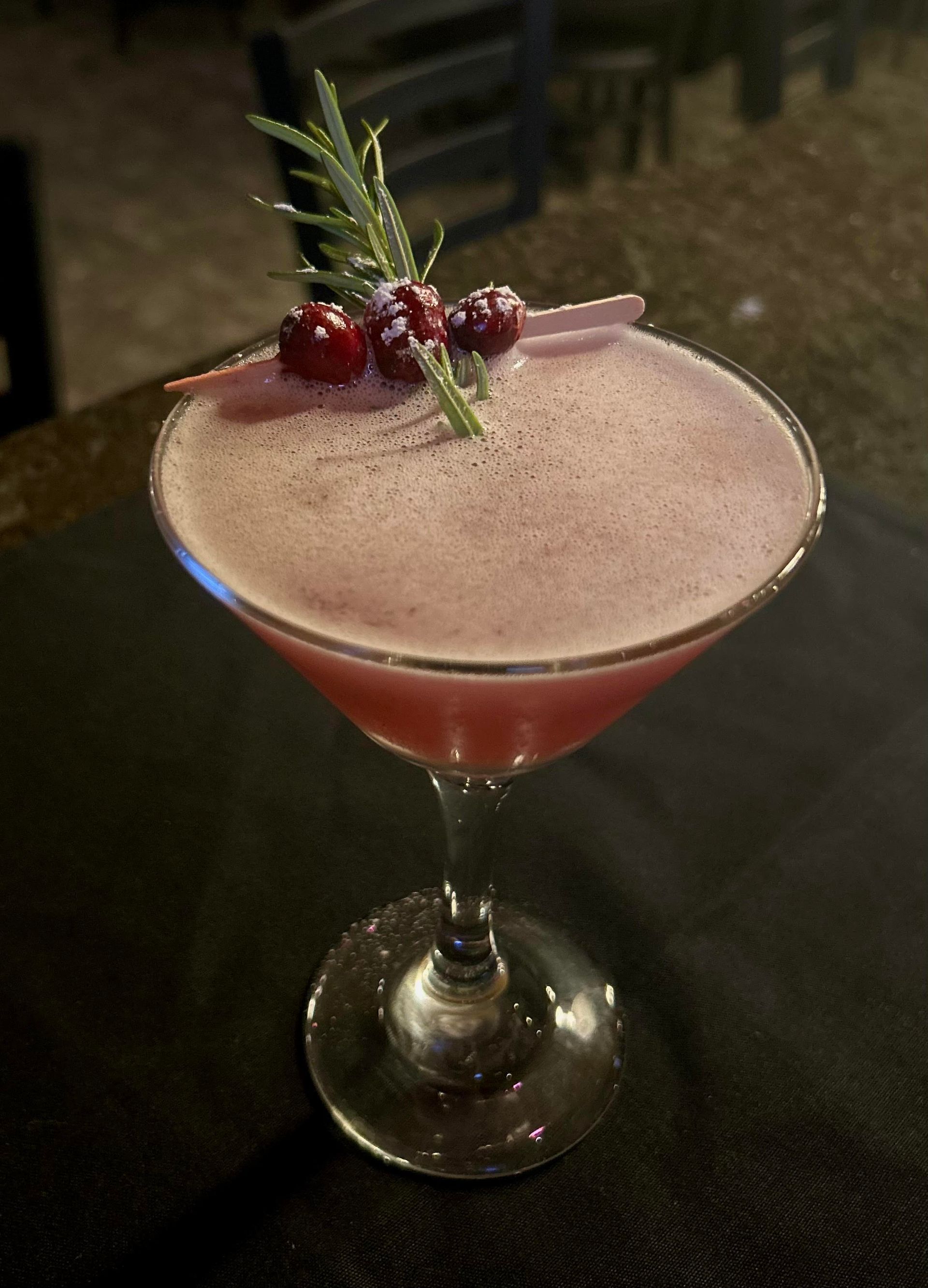A martini with cranberries and rosemary on top of it