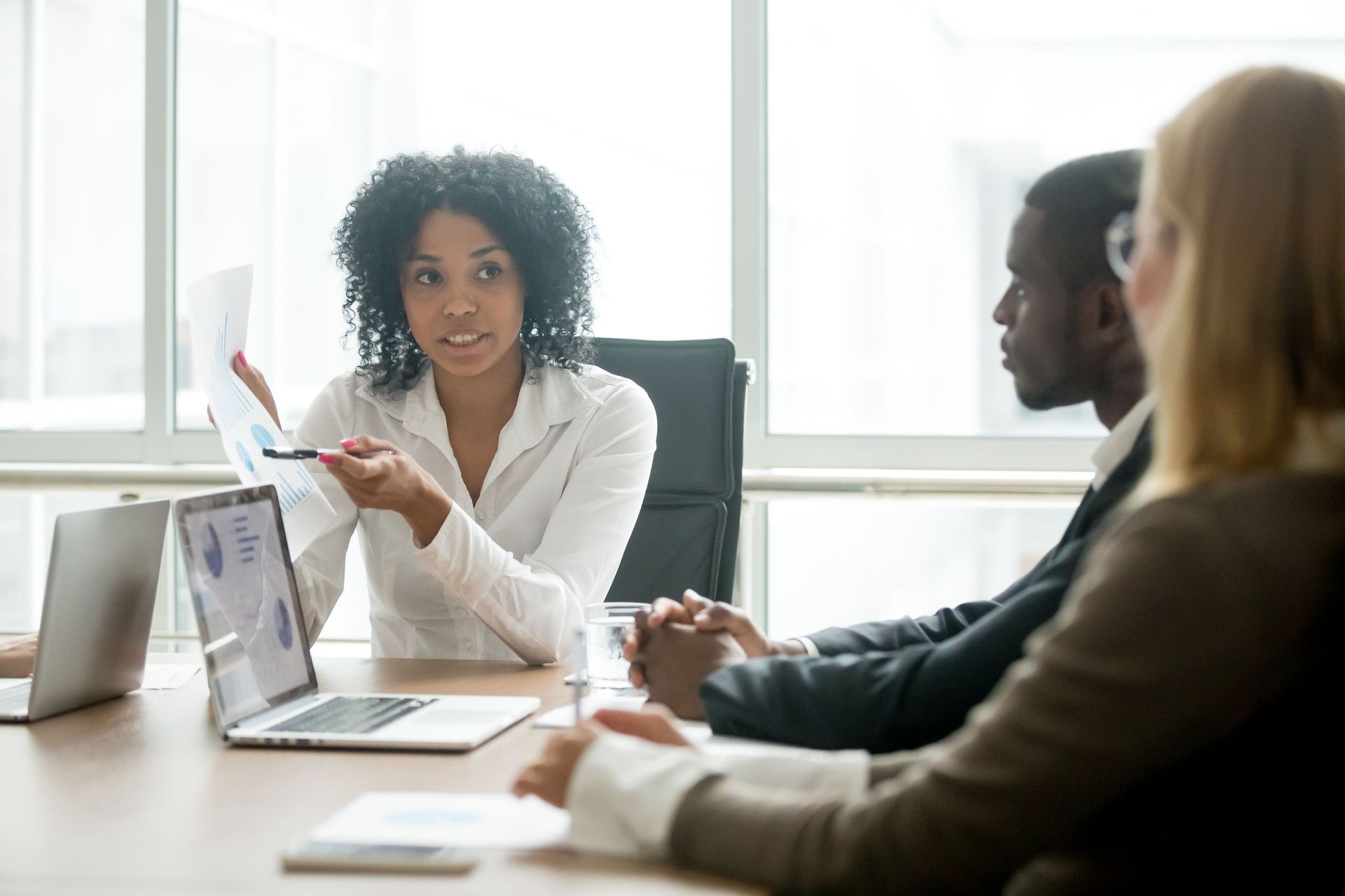 Small business meeting in a bright office, with one person presenting to two colleagues at a table.