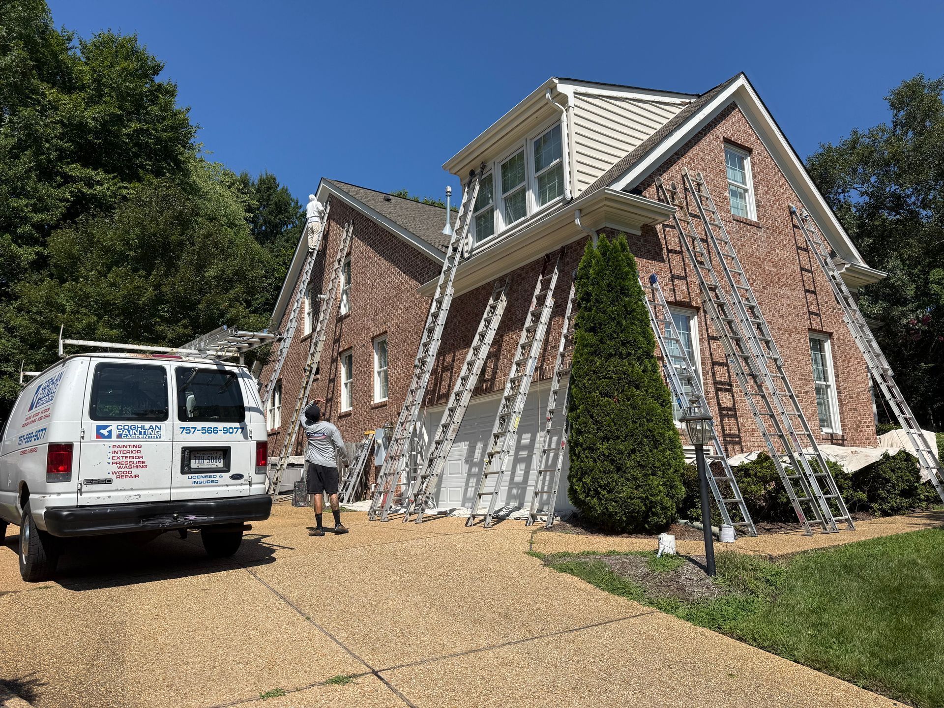 House under repair with ladders leaning against brick walls and a work van in the driveway