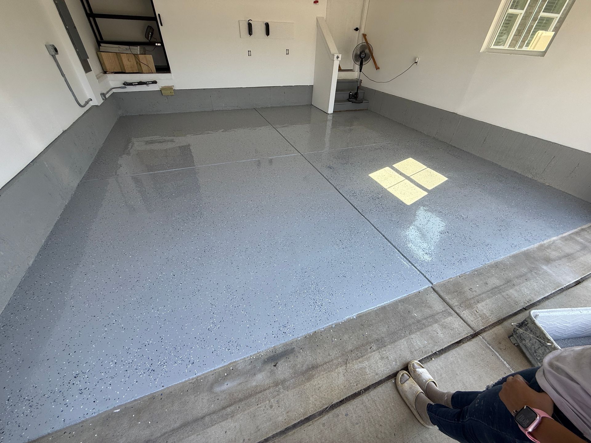 Empty garage with speckled gray epoxy floor and sunlight from windows on the right.