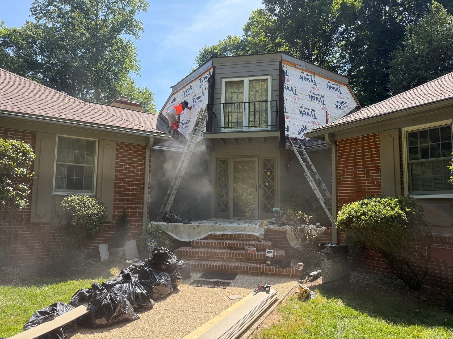 Firefighters spray water at a two-story house with smoke and charred debris at the entrance.