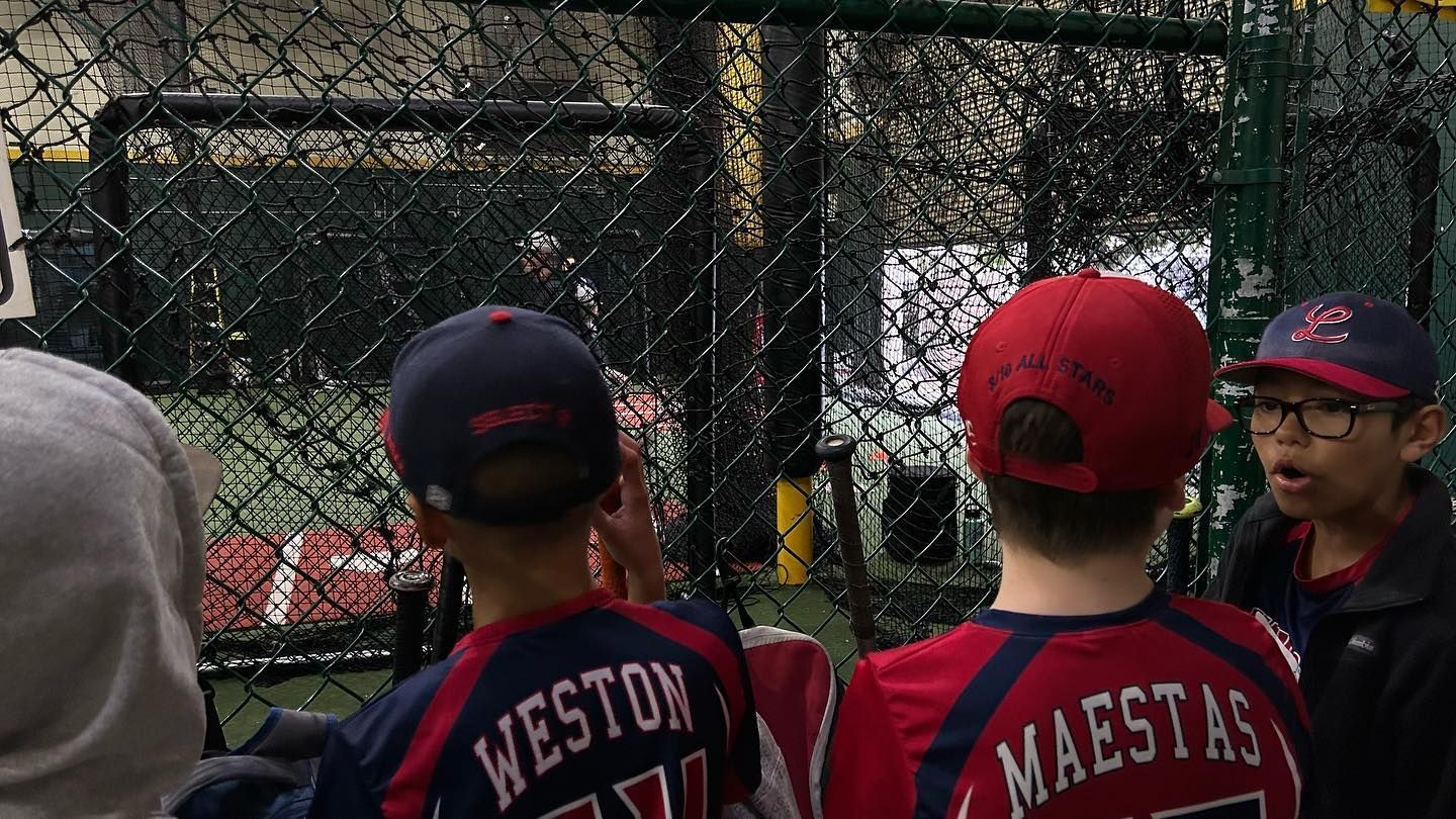 A group of young boys are watching a baseball game in a cage.