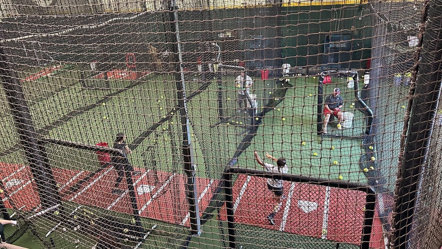 A group of people are playing baseball in a cage.