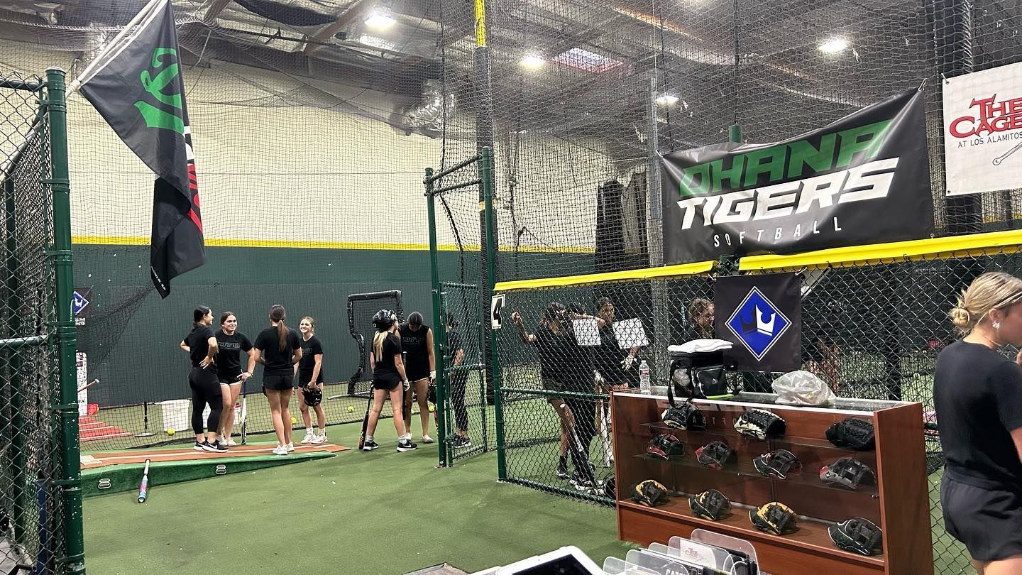 A group of people are standing in a baseball cage.