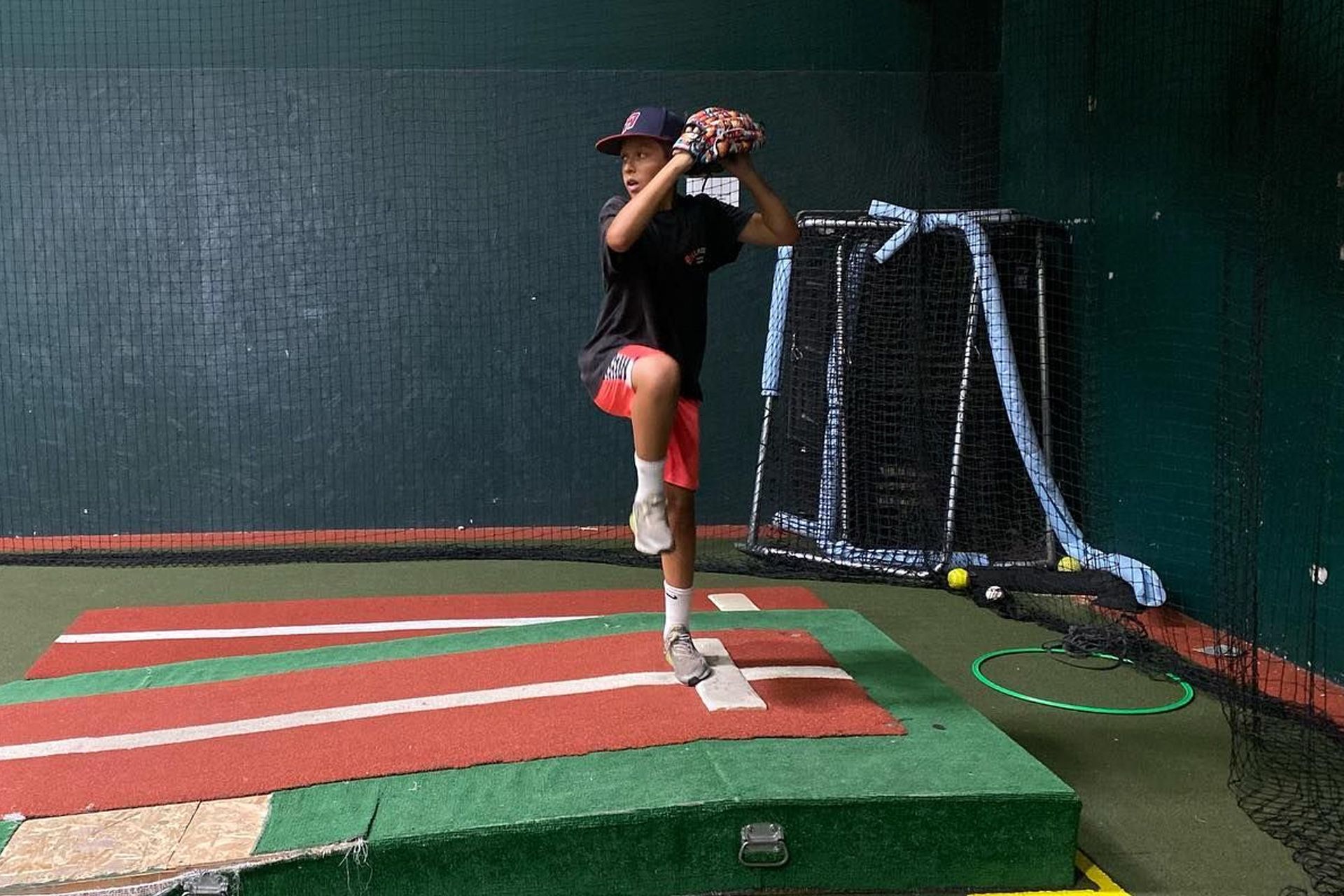 A young boy is pitching a baseball in a baseball cage.