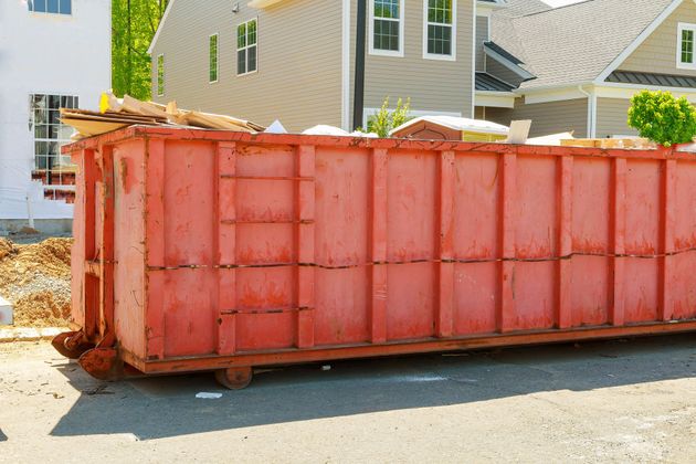 Red construction dumpster filled with debris on a residential street