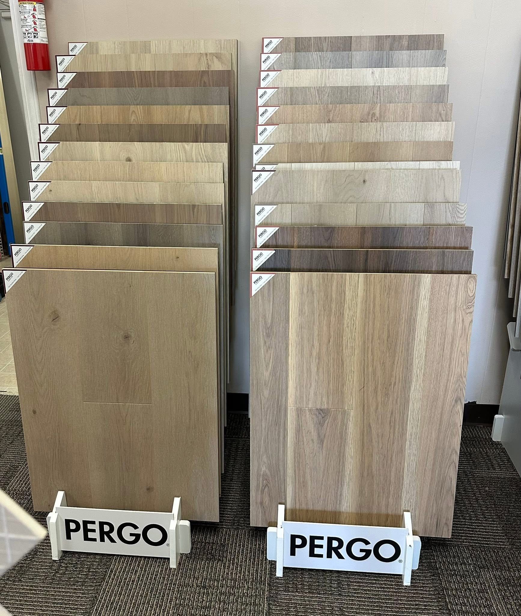 Two displays of PERGO flooring samples in neutral tan, gray, and wood tones side by side on stands