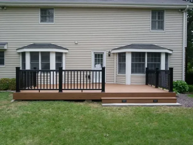 Brown deck with black railing, connected to a beige house, in a grassy yard.