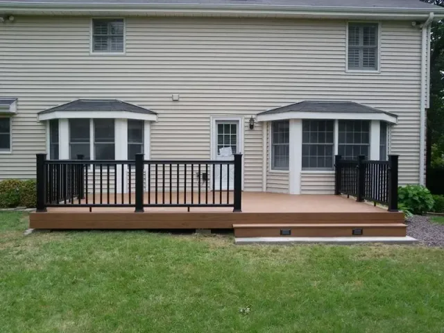 Brown deck with black railing, connected to a beige house, in a grassy yard.