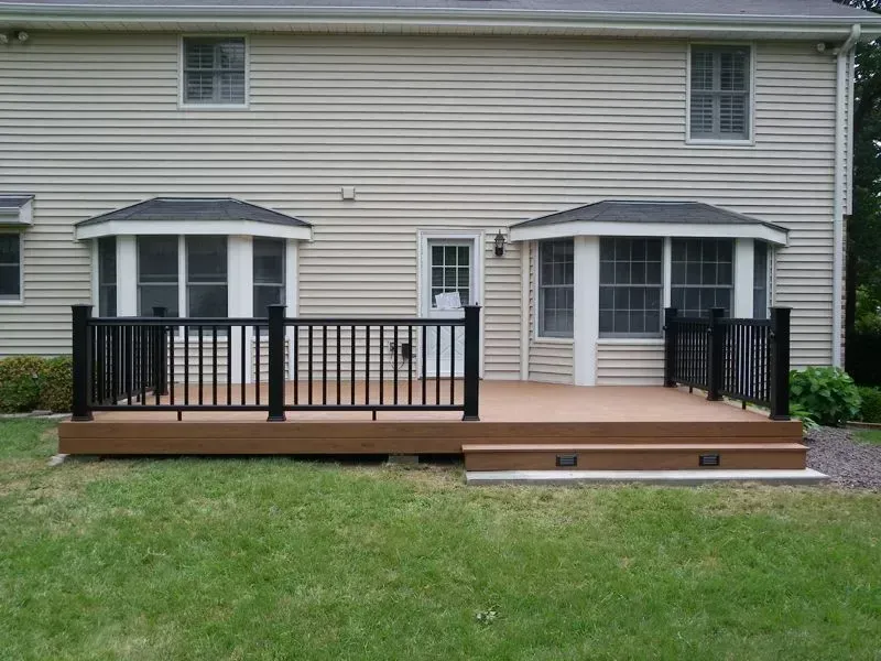 Backyard deck with black railing and steps attached to a beige house