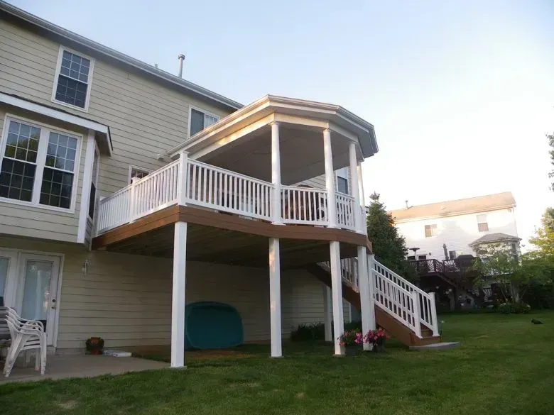 Raised wooden deck with white railings and stairs attached to a beige house in a backyard