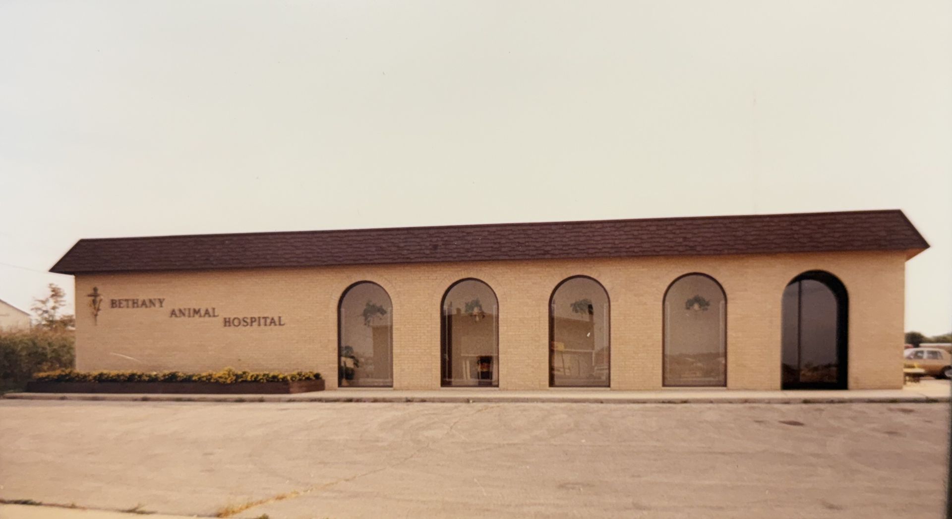 Long, tan stucco building with arched doorways and a dark roof in a sandy lot.