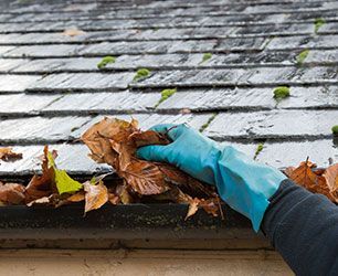 Gloved hand clearing leaves from a gutter on a roof.