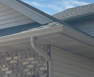 Gray gutters and downspout on a house with brick and gray siding.