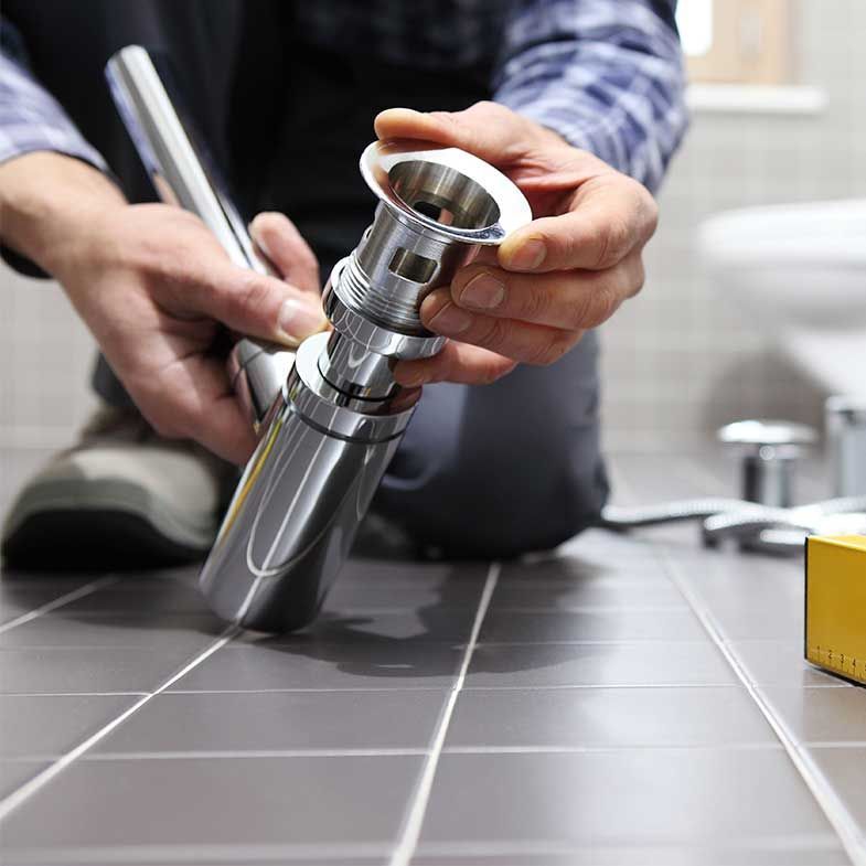 A man is kneeling down fixing a faucet in a bathroom