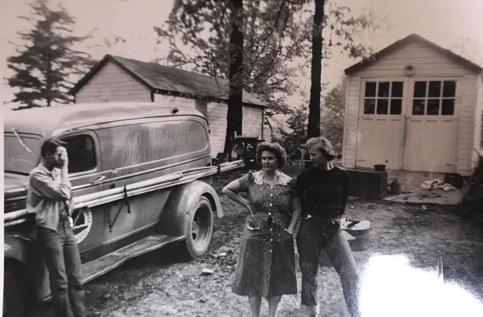A black and white photo of three people standing in front of an old truck