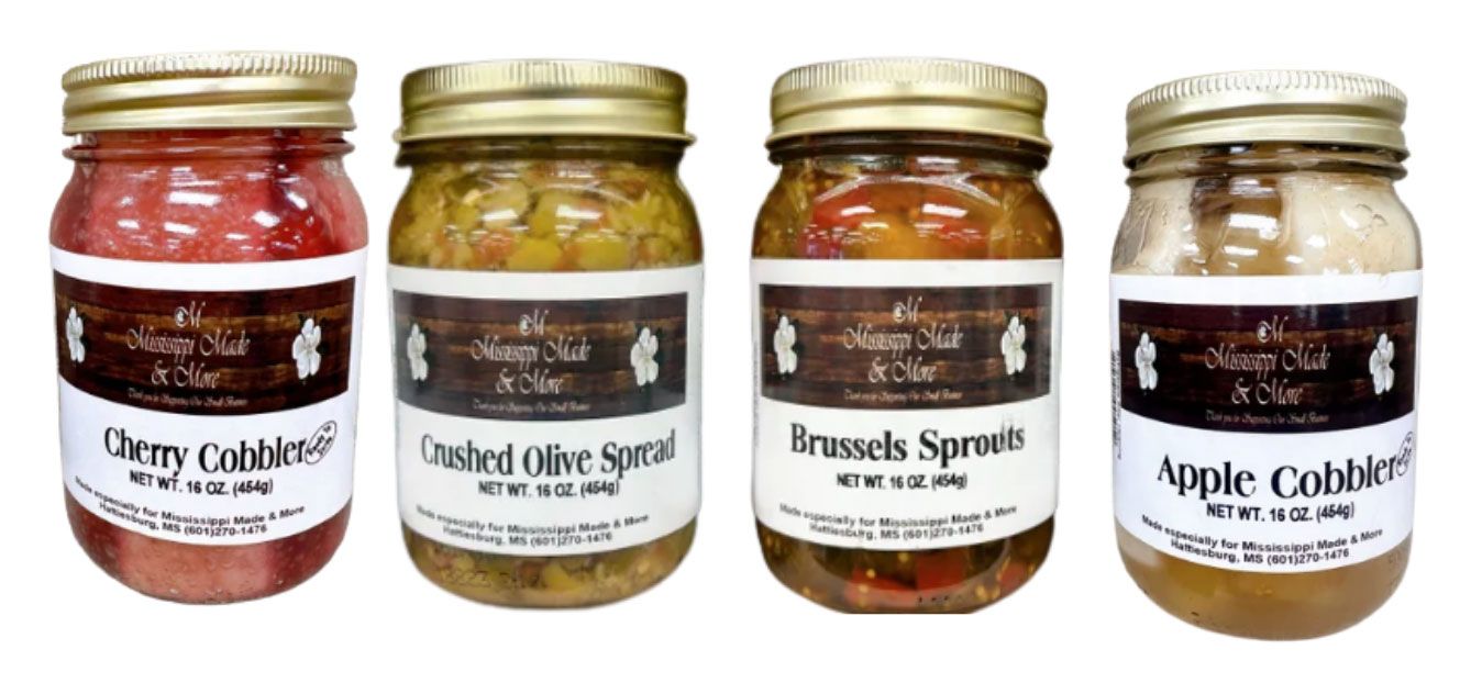 Four jars of homemade preserves with gold lids and white labels, including cherry cobbler and apple cobbler.