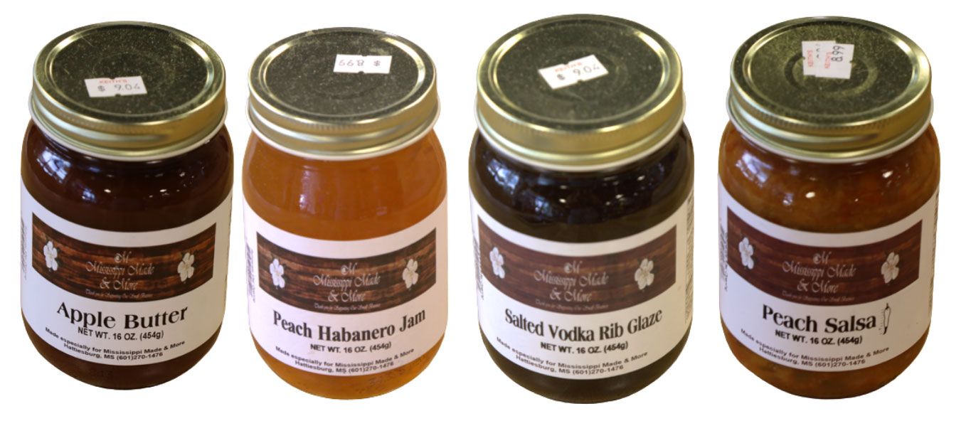 Four jars of assorted sauces with gold lids, labeled and arranged in a row on a white background